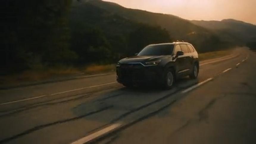 Black suv car traveling down a road surrounded by mountains with golden sun on the horizon
