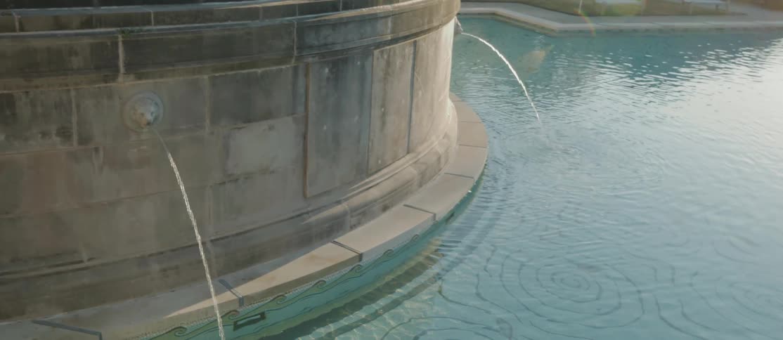 Closeup view of a water fountain with water arching from a spout on the side of a stone structure