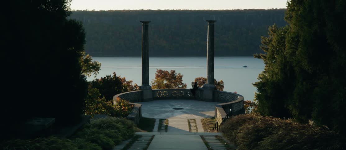 A circular neoclassical structure with two tall columns overlooks a calm lake