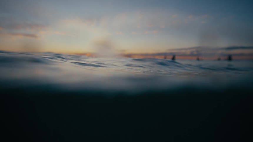 Close up view of calm ocean surface during sunrise with surfers