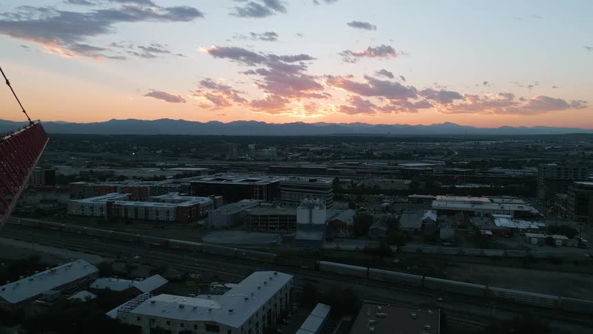 From the lofty vantage point of a construction crane the city skyline unfolds beneath a breathtaking sunset with distant mountains silhouetted against the fiery sky