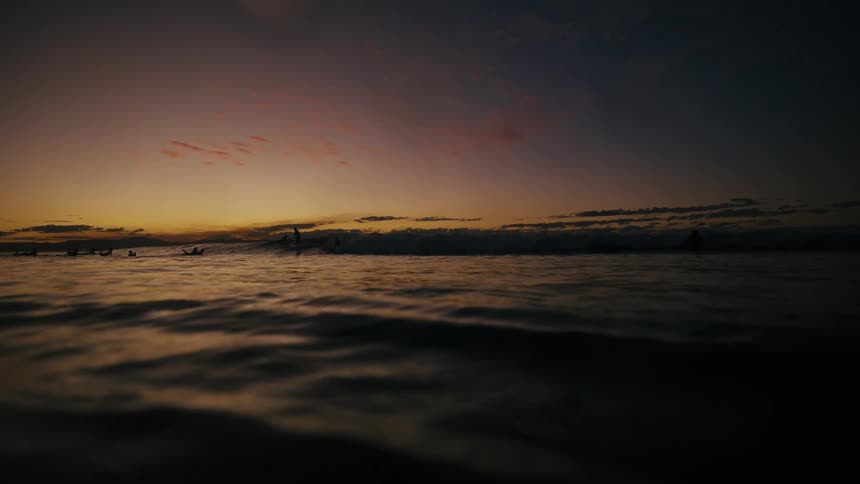 Sun reflects on the water and silhouette of surfers in the sea