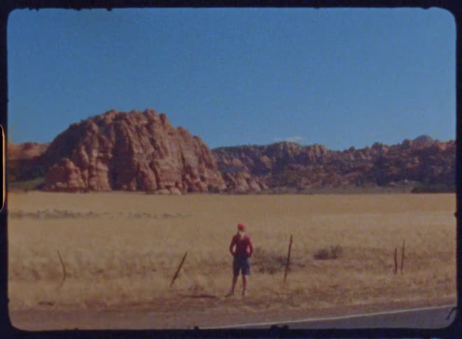 A woman stands on the roadside gazing at vast grassland plains and rocky mountains captured on vintage film