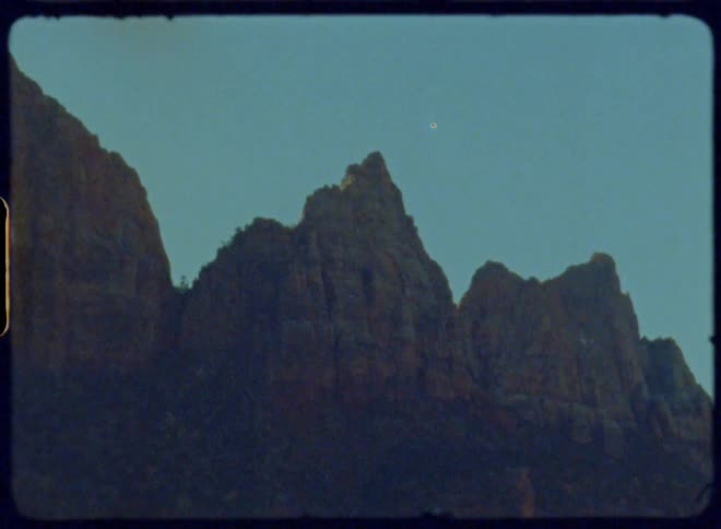 A rocky mountain peak rises against a clear blue sky captured on vintage film