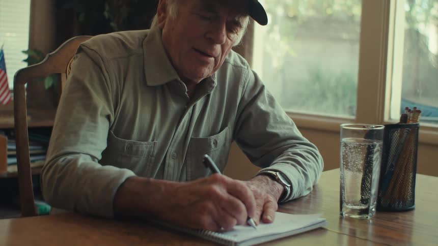 A clip of an elderly person writing on a book