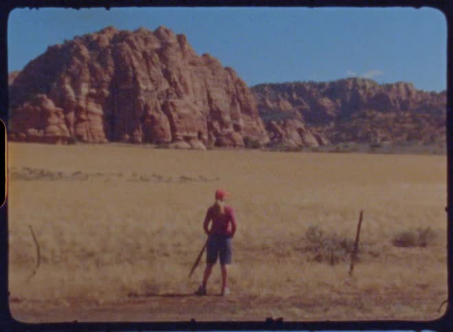 Woman dressed in red in a field with a large rock formation in the background under a clear blue sky