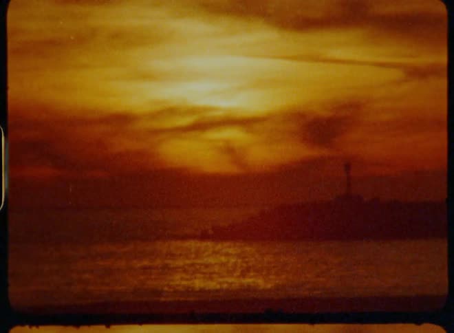 The sun sets over a body of water casting a warm orange glow captured on vintage film