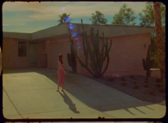 Woman is standing on a concrete path leading to a building with large cacti