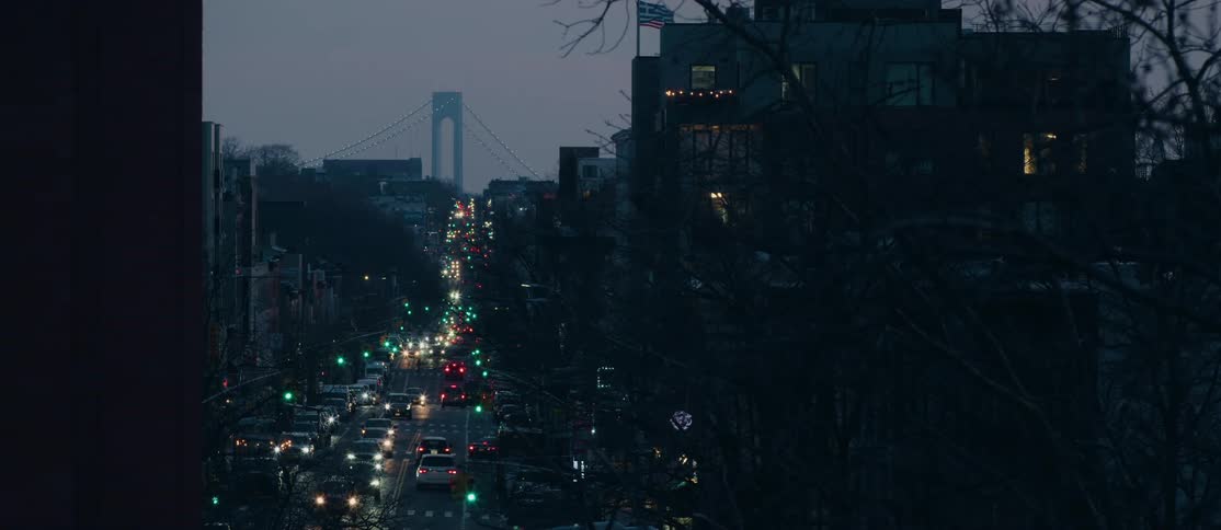 A bustling city street illuminated by streetlights with a bridge visible in the distance
