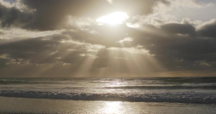 The sun breaks through the clouds casting beams of light across the rippling ocean waves creating a breathtaking sight