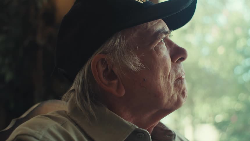 An elderly man with a concerned expression writes at home