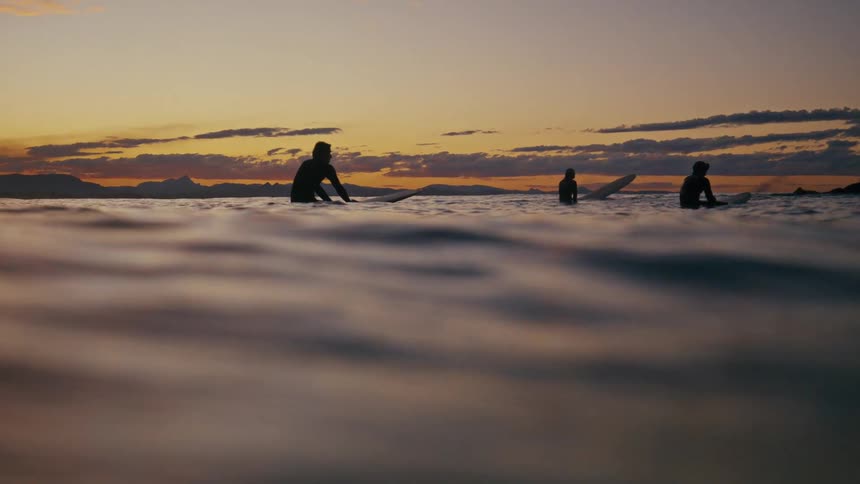 Silhouette of surfers on surfboards floating in a calm ocean at sunset