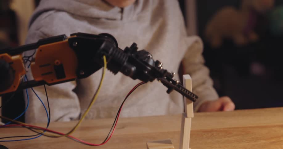 Boy working on a project on a mechanical hand that tries to balance two pieces on top of each other