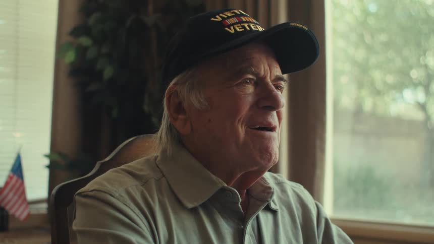 An elderly man writing a letter looks up with a happy daydreaming expression