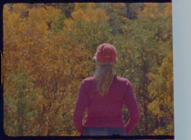 A woman in a pink shirt and hat gazes at an autumn colored forest captured on vintage film