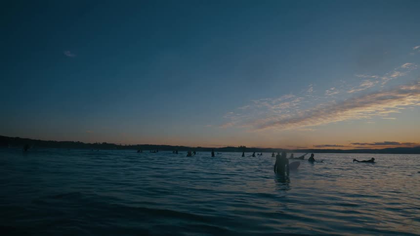 A group of surfers floating in the ocean during sunset
