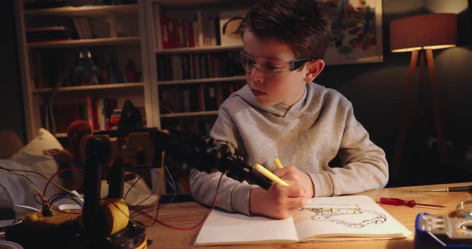 Boy is at a table working on an electronics project with a soldering iron in his hand and components scattered around