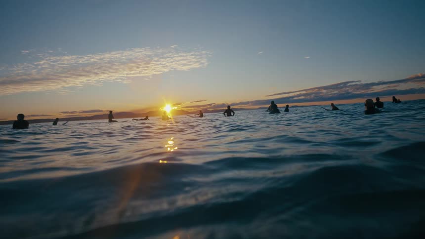 Silhouetted surfers patiently await the perfect wave their figures bathed in the golden glow of the setting sun