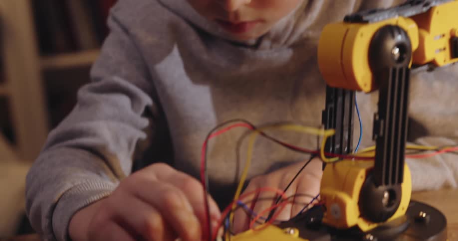 Closeup of a concentrated boys hands working on an electronic device with a robotic arm and wires