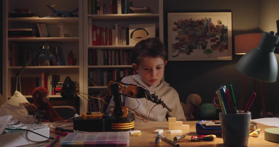 Concentrated boy working on a mechanical hand that balances objects on the table