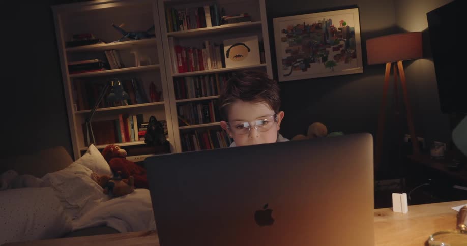 A boy sits at a desk with a laptop in a cozy livingroom