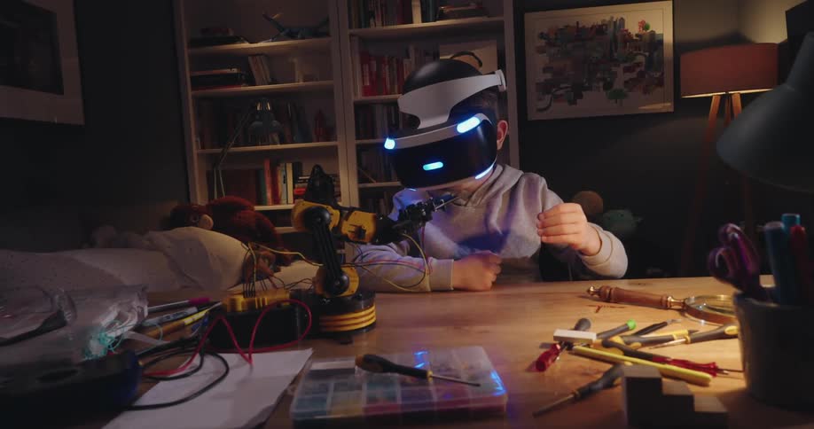 A boy wearing vr goggles operates a small robotic arm on a desk