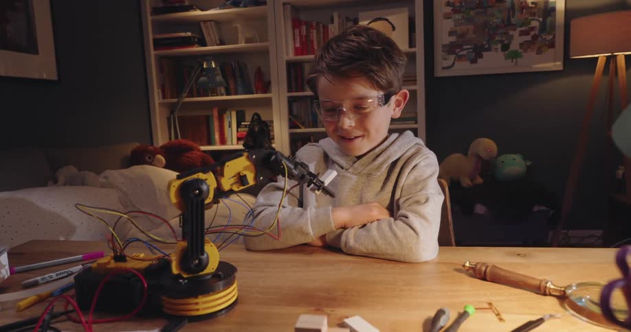 Boy is sitting at a table with several electronic components and a mechanical arm
