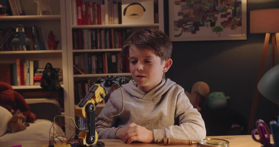 A boy interacts with a small robotic arm over a desk at home
