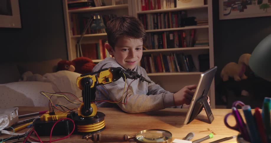 A child uses a tablet to program a small robotic arm and celebrates when it moves