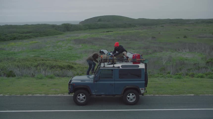 Two men stand on top of a vehicle that is parked roadside