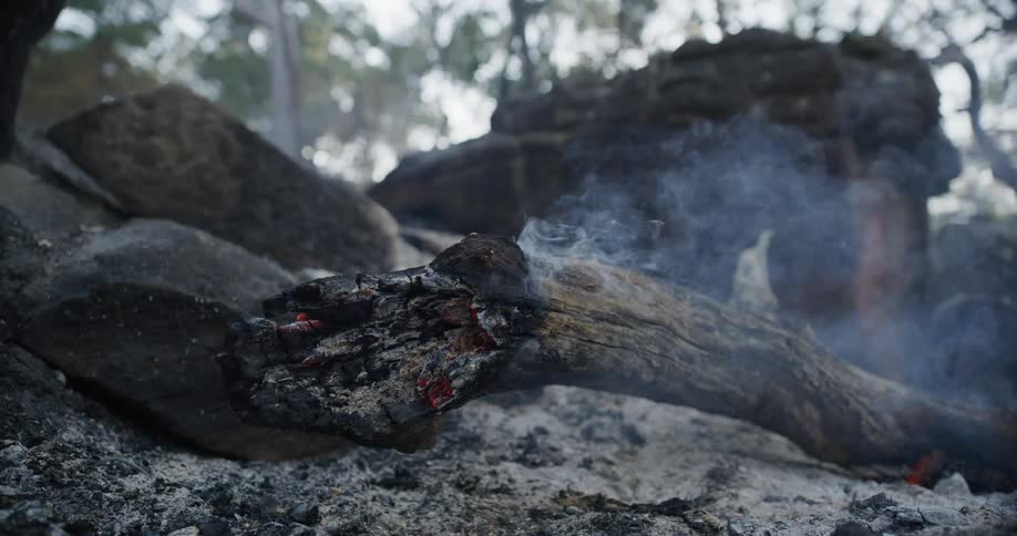 Piece of wood with glowing embers emitting smoke among rocks and ash