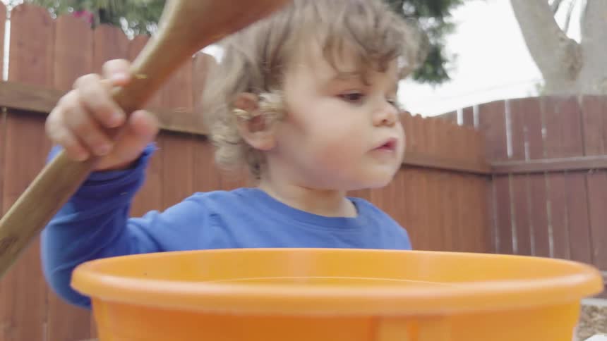 Mother guides her child while the young boy scoops seeds and pulp out of pumpkins in their backyard