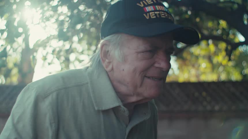 Elderly man walking through the yard and smelling a pink flower
