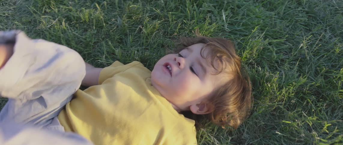 Young redheaded child lies on the grass and lifts their legs