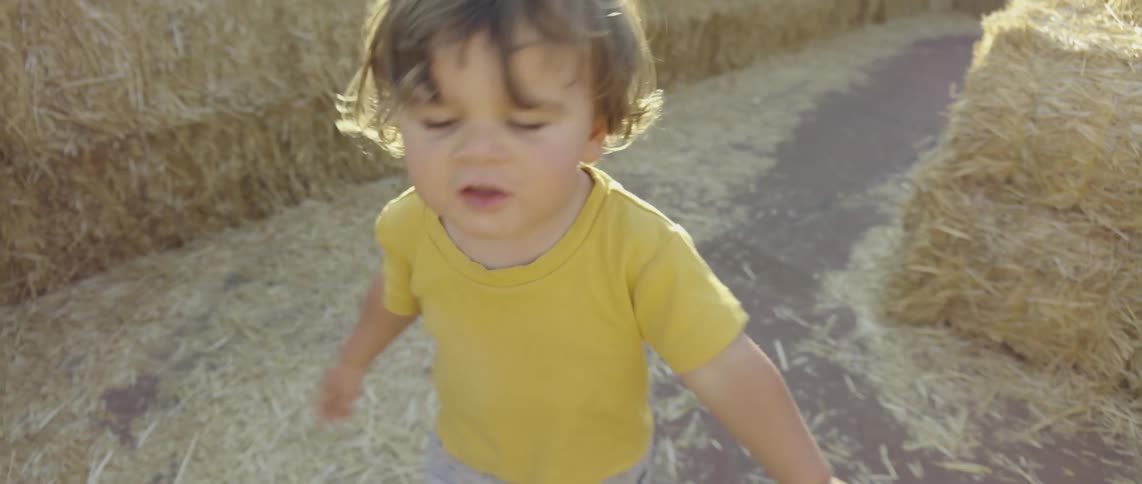 A toddler walks through a maze made out of hay bales
