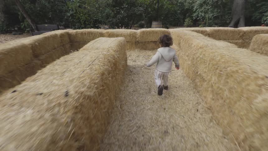 Young child runs through a maze made of stacked straw bales
