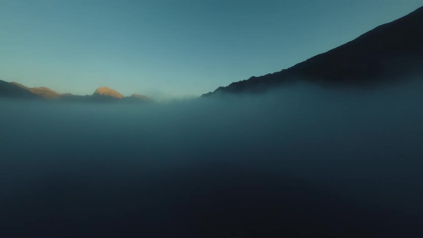 Aerial clip of dense fog fills a mountain valley at sunset / sunrise