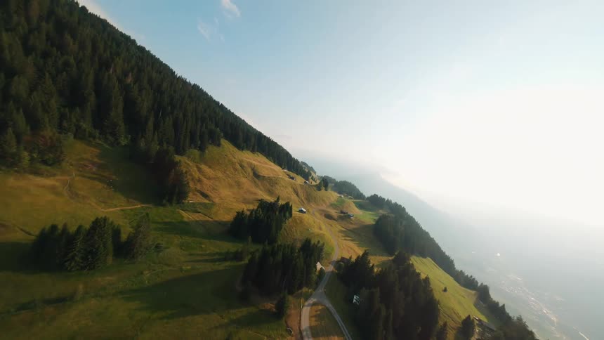Small mountain road passes through a rural town bordered by forest on a mountain towering over a foggy valley in Switzerland