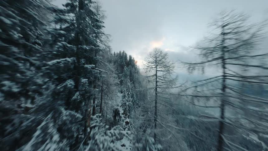 A drone flies over a snow covered mountainside revealing a valley shrouded in fog