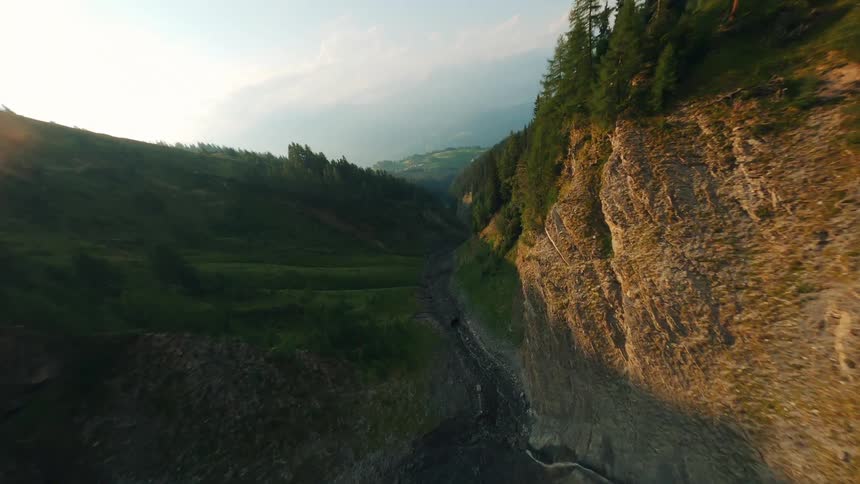 A drone flies through a narrow valley between steep tree covered mountainsides in switzerland