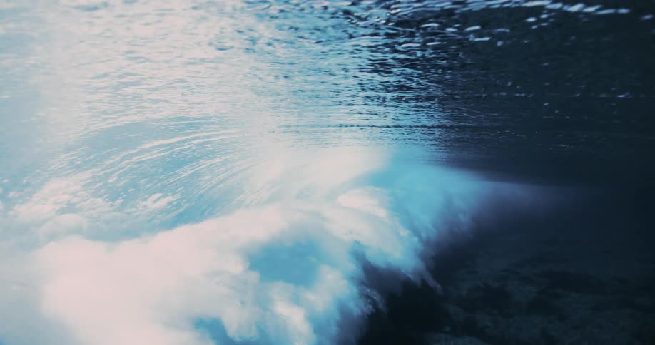 An underwater shot shows a wave breaking above creating churning whitewater and bubbles