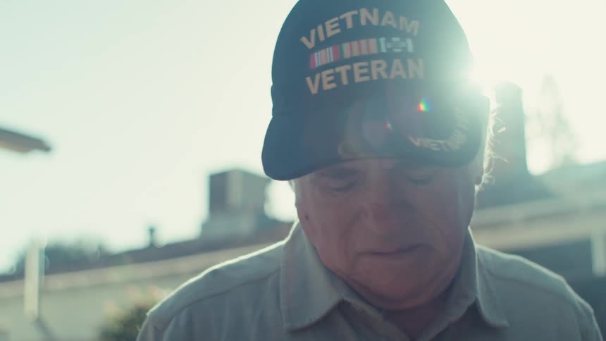 Glaring sunlight temporarily obscures the face of an elderly veteran standing in his yard
