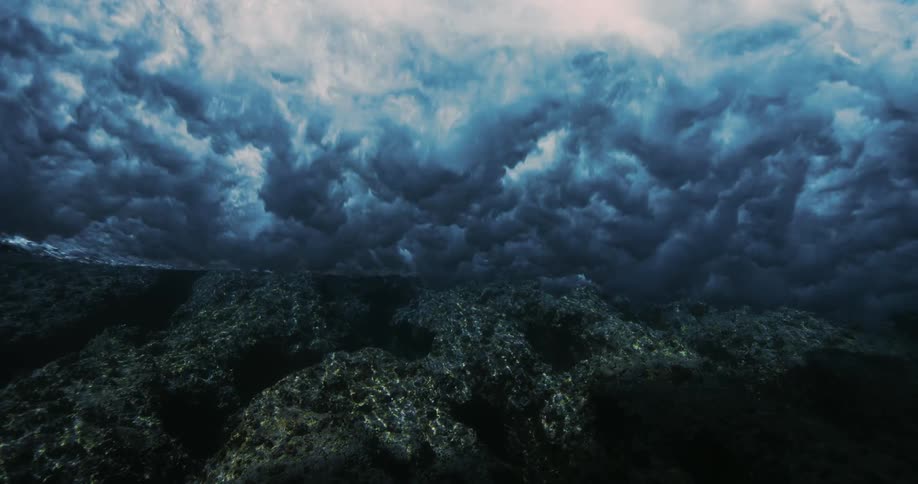 A large wave crests above coral reefs near a coast