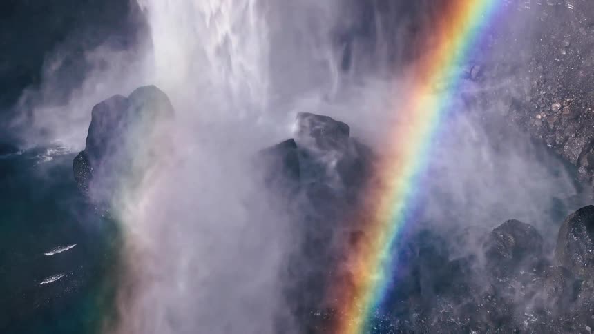 Majestic waterfall cascades down the cliff form a vibrant rainbow