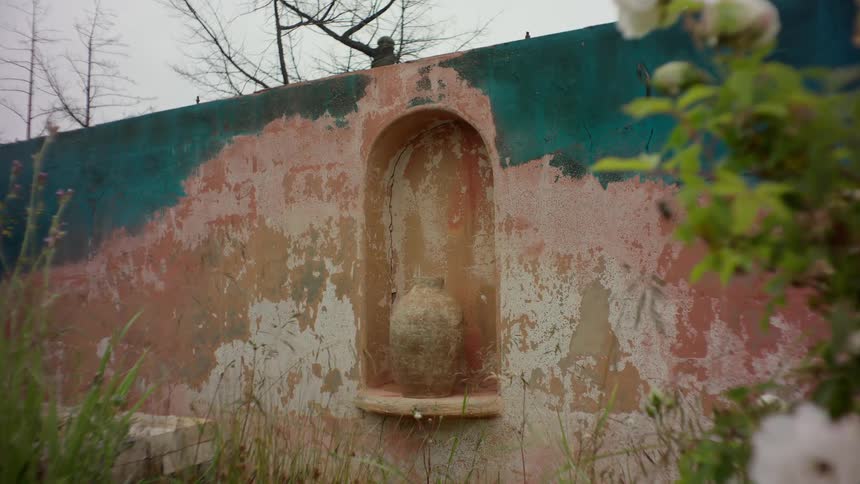 A small arched niche in a weathered wall holds a ceramic pot the wall is painted in shades of blue and pink