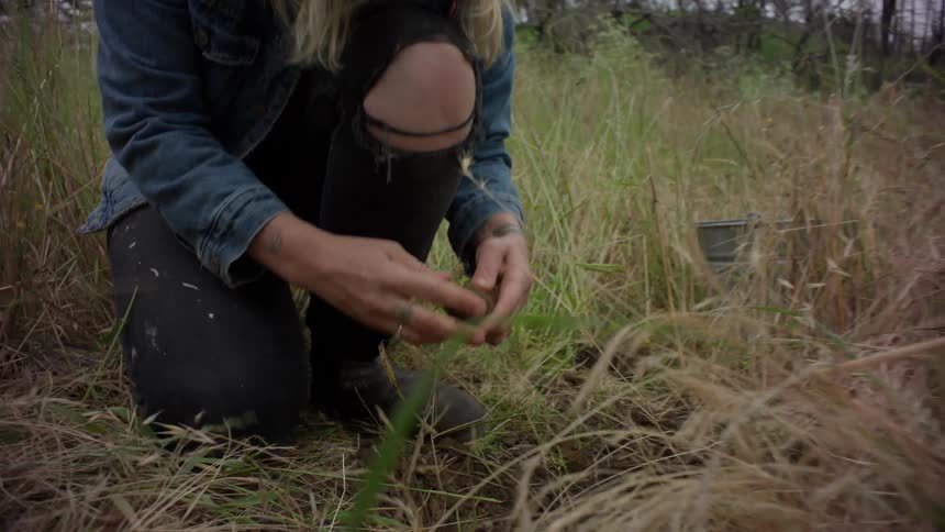 Woman in a field with tall grass scooping clay from a hole