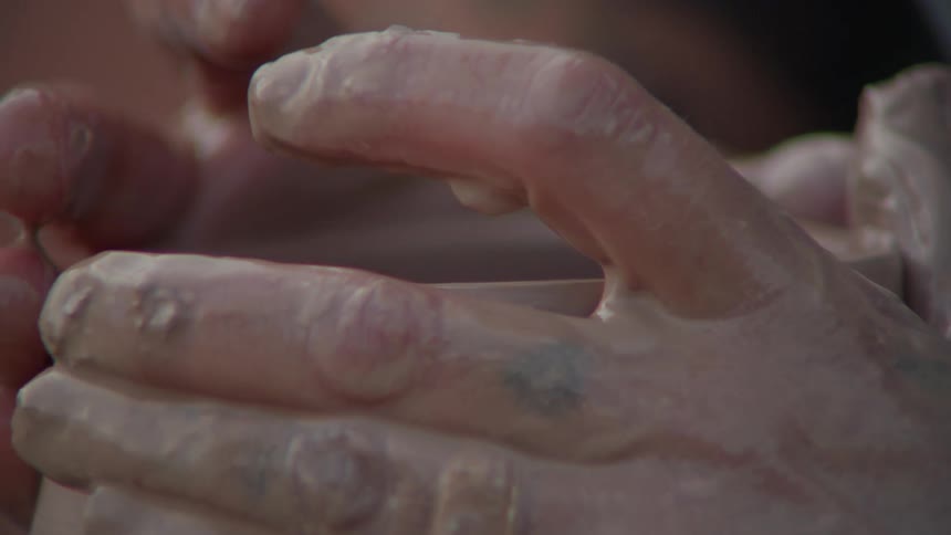 Closeup of hands shaping a clay vase on a turning table