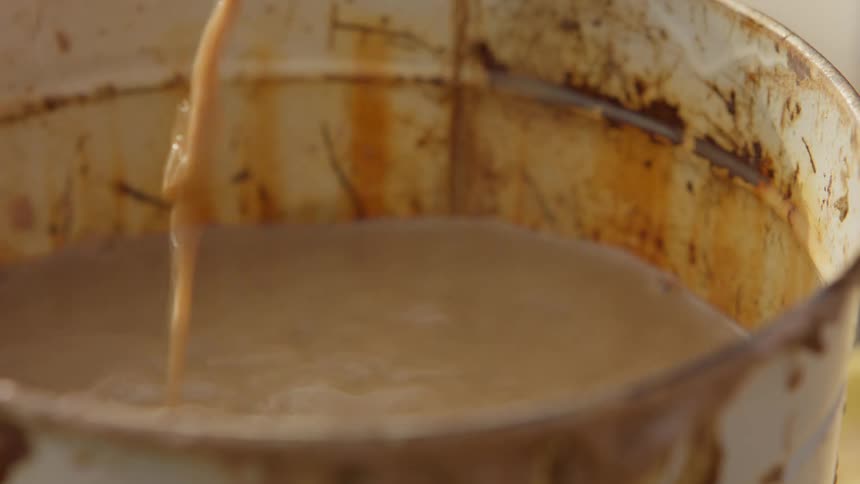 A hand retrieves a sponge from a bucket of muddy water