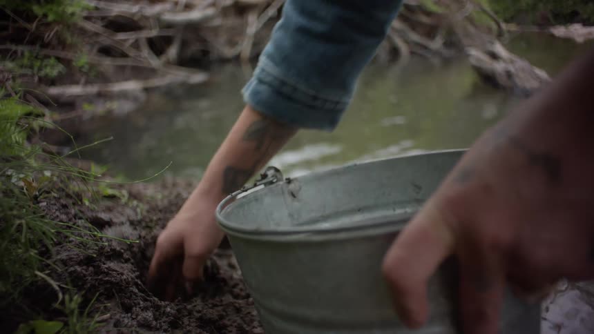 Man examines mud dug from a stream bank and places it into a metal bucket