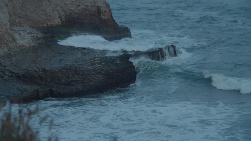 Ocean waves crash against a rocky cliff edge